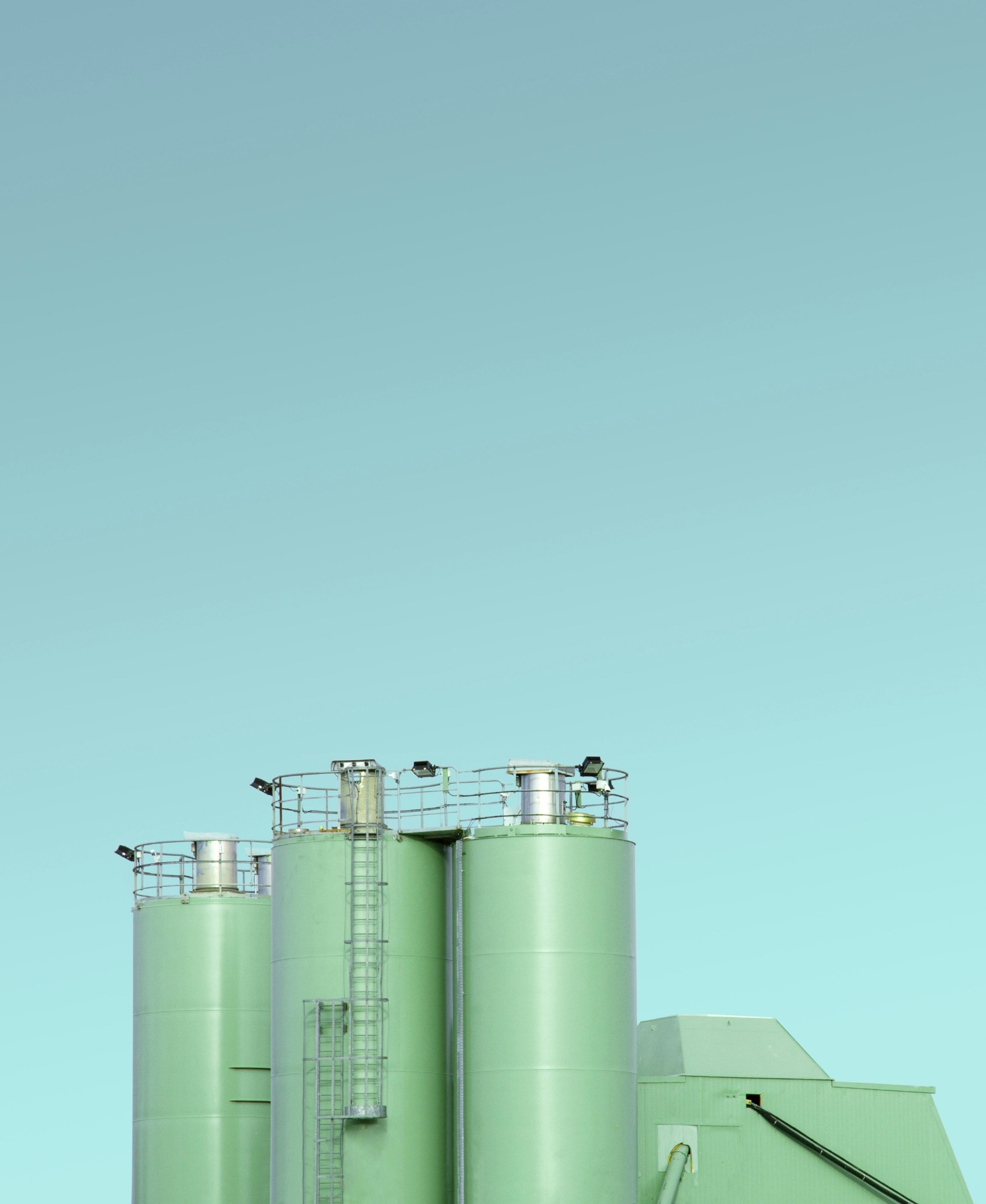 Industrial green storage silos against a clear sky